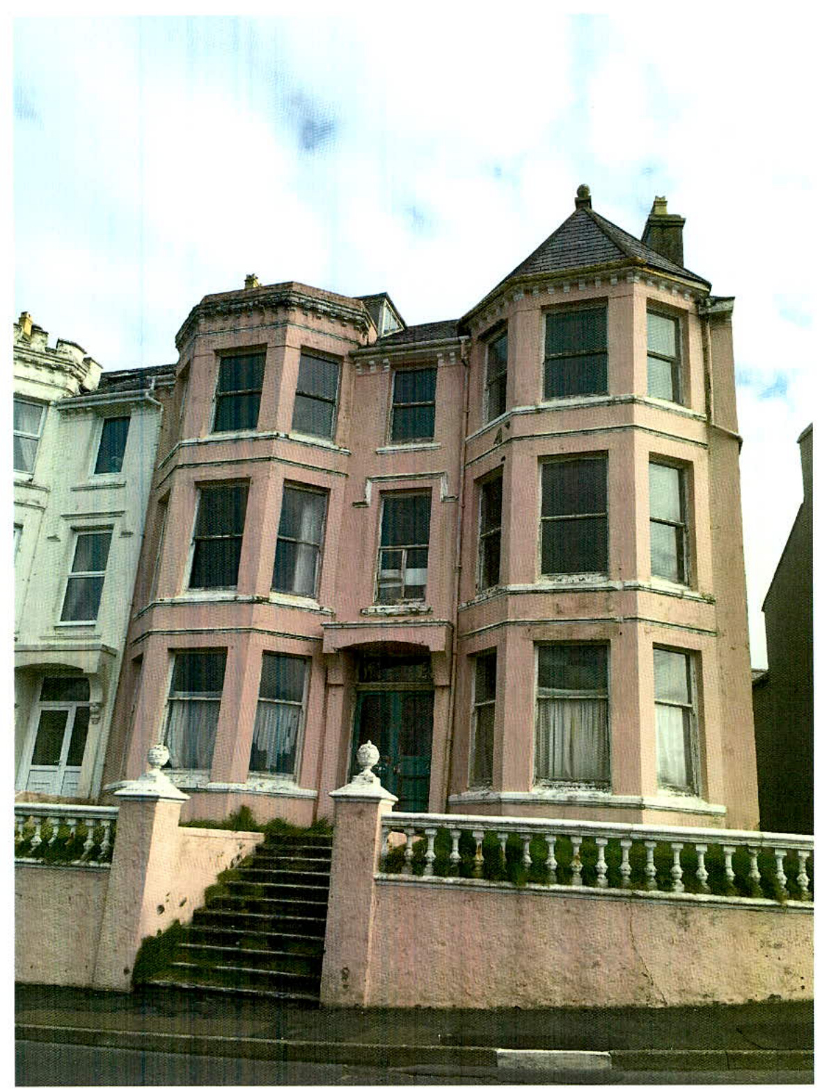 A street-level photograph of a large, three-story pink building with bay windows and a balustrade, identified as a former guest house.