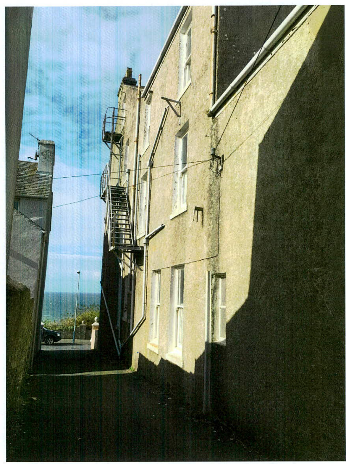 A low-angle photograph showing the side elevation of a tall, rendered terraced building with an external metal fire escape staircase.