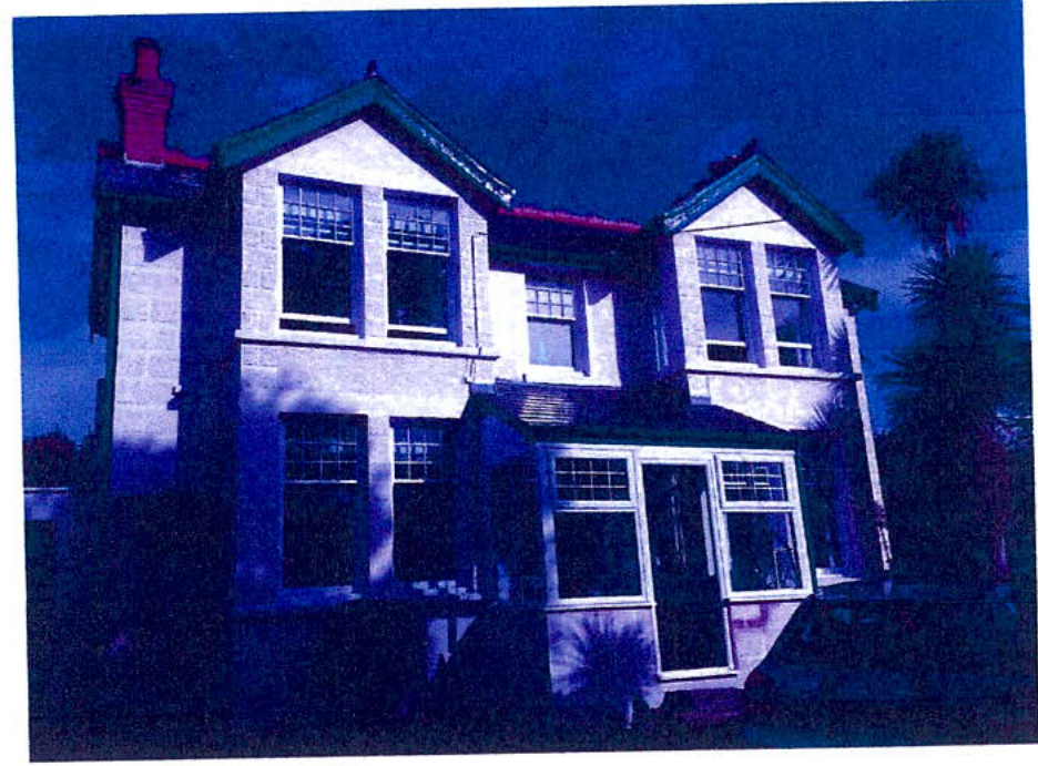 A blue-tinted photograph showing the exterior of a two-story detached house with a conservatory extension.