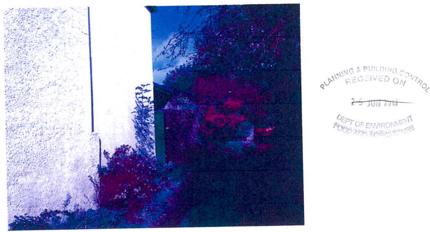 A color-inverted, low-quality photograph showing the exterior wall and garden vegetation of a property, with a planning department receipt stamp on the right.