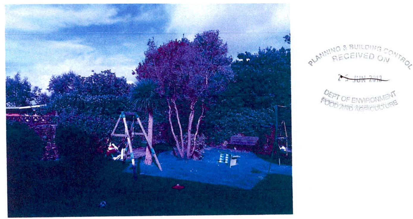 A photograph of a residential rear garden featuring a swing set, trees, and a bench, with an official Planning & Building Control received stamp on the right.