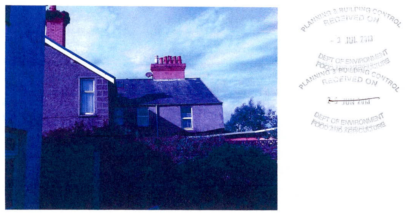 A photograph of an existing stone residential property showing the roofline, chimney stack, and surrounding boundary vegetation, likely documenting the current state for a planning application.