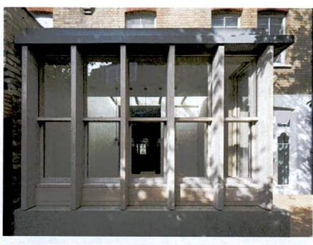 A photograph showing a glazed extension or porch structure attached to the side of a brick building.