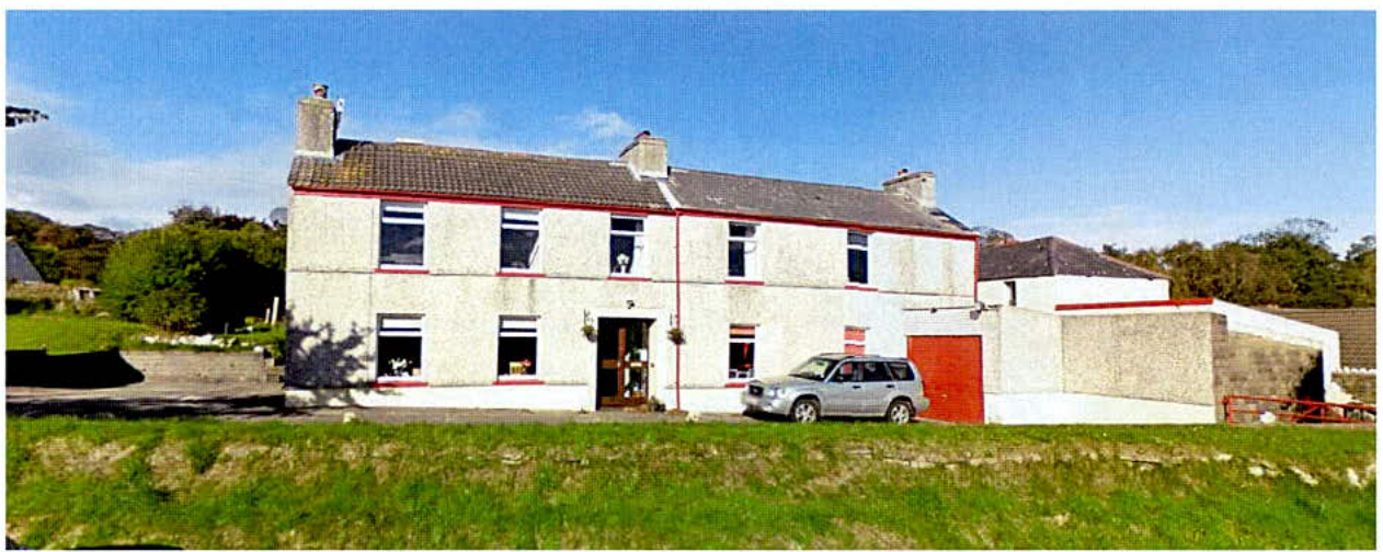 A photograph showing a large white two-story detached house with a red garage door and a car parked on the driveway in a rural setting.