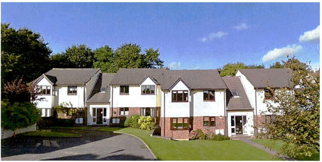 A row of modern white and brick residential houses with grey tiled roofs and surrounding green landscaping.