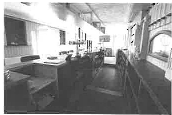 A black and white photograph showing the interior of a public house, featuring a long bar counter on the right and a service area on the left.