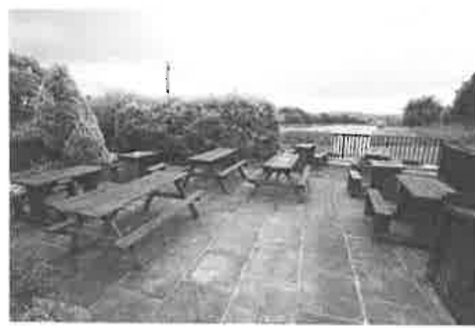 Black and white photograph showing an outdoor patio area furnished with wooden picnic tables and benches, likely the beer garden of the public house.