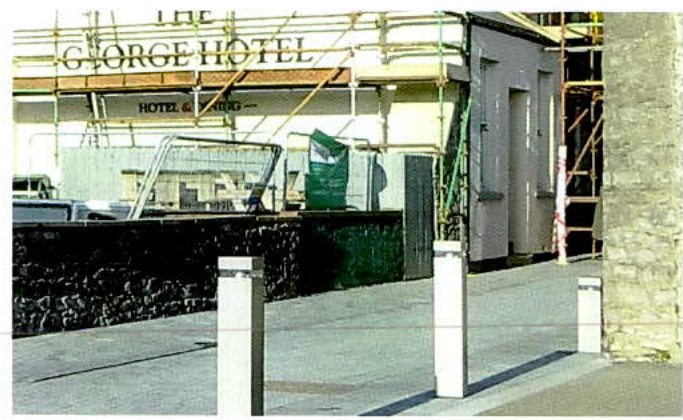 A photograph showing the exterior of 'The George Hotel' with scaffolding erected around the upper levels and a stone wall in the foreground.