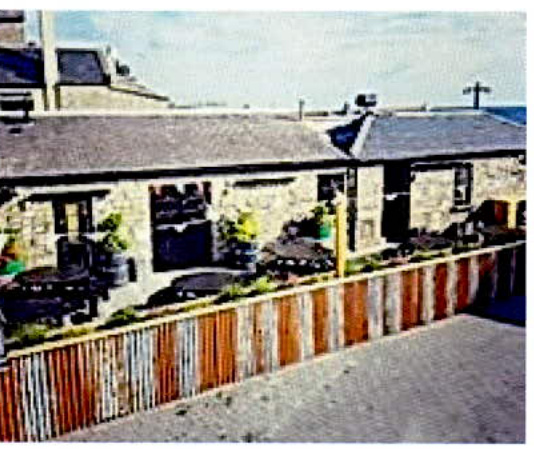 A photograph showing the rear of a stone building with a patio area and a new wooden fence in the foreground.
