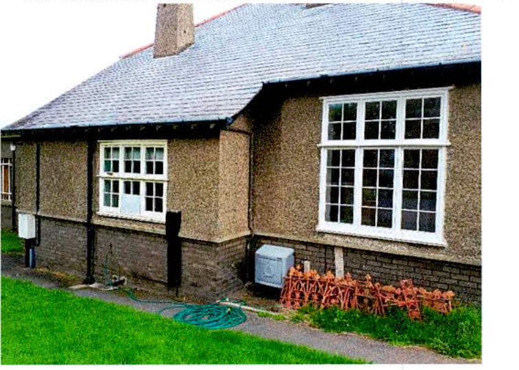 Exterior photograph of a single-story bungalow with pebbledash walls and white replacement windows.