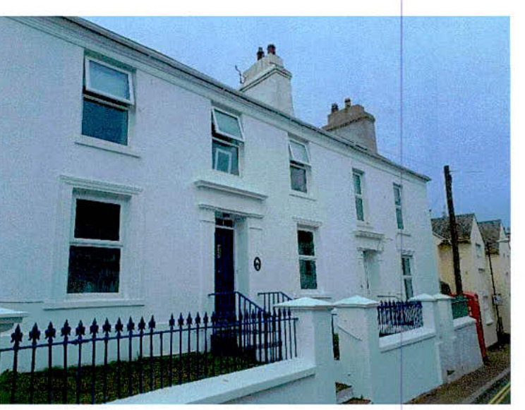 A photograph showing the front elevation of a white, two-story terraced house with open windows and a black metal railing along the boundary.