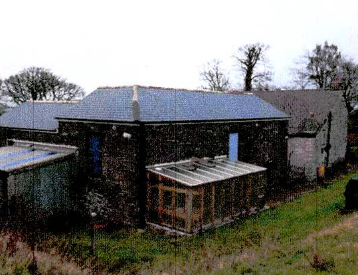Grainy exterior photograph of a stone outbuilding with a slate roof and an attached lean-to extension in a rural setting.