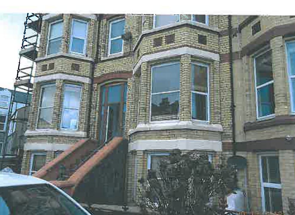 A photograph showing the front elevation of a yellow brick terraced house with bay windows and scaffolding on the left side.