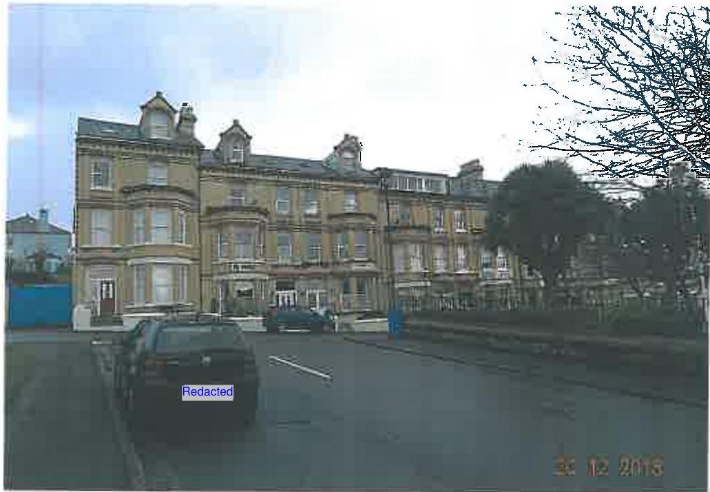 A street-level photograph showing a large, multi-story terraced building with bay windows and dormers, with a car parked in the foreground.