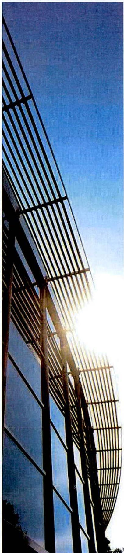 A low-angle photograph showing the upper facade of a modern building featuring horizontal slatted screening and glass panels against a bright blue sky.
