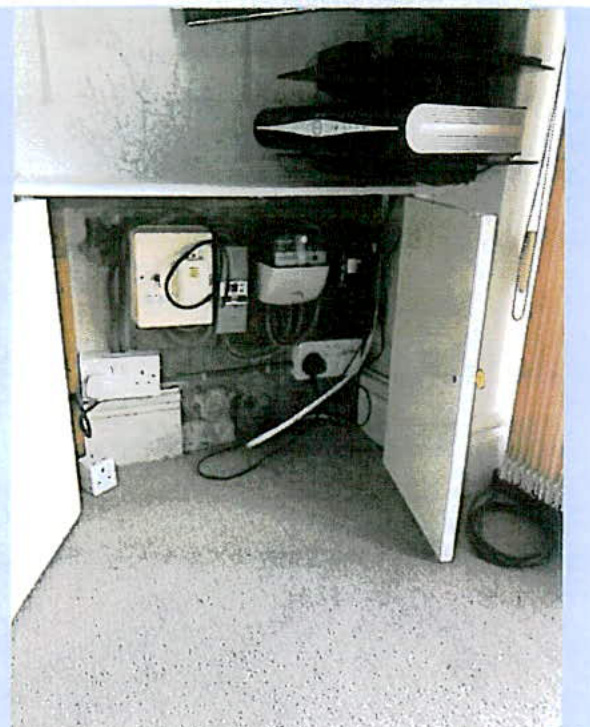 A photograph showing the interior of a utility cupboard containing electrical meters, fuse boxes, and wiring.