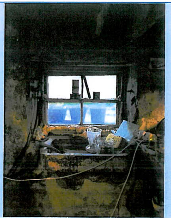 A grainy interior photograph showing a room with a window, distressed walls, and a sink area, likely documenting existing conditions for renovation.