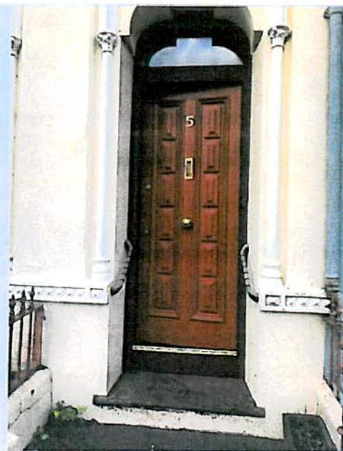 A close-up photograph of a residential front entrance featuring a wooden double door with the number 5, set within an arched doorway flanked by white columns.