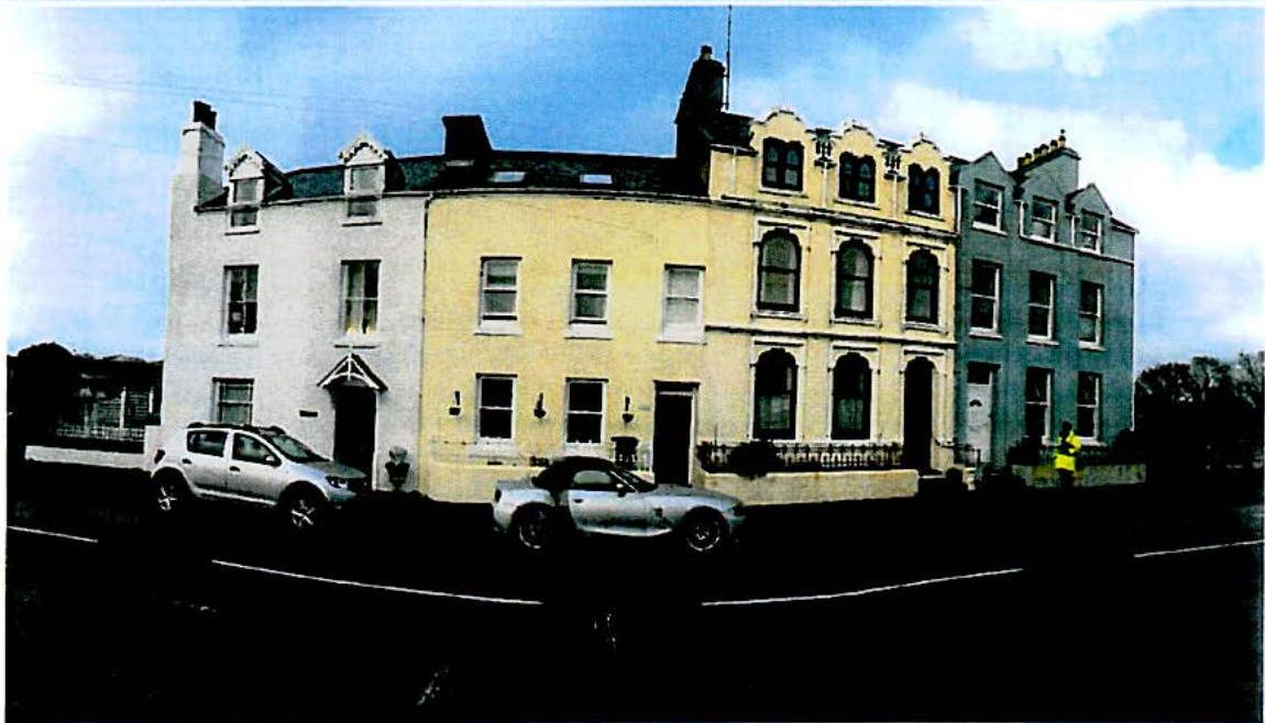 A street-level photograph showing a row of terraced houses, focusing on a central cream-colored building with cars parked on the street.