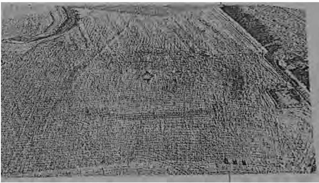 A grainy, black and white aerial photograph showing a large expanse of rural land or field with visible tracks, likely depicting the site of the proposed residential development.