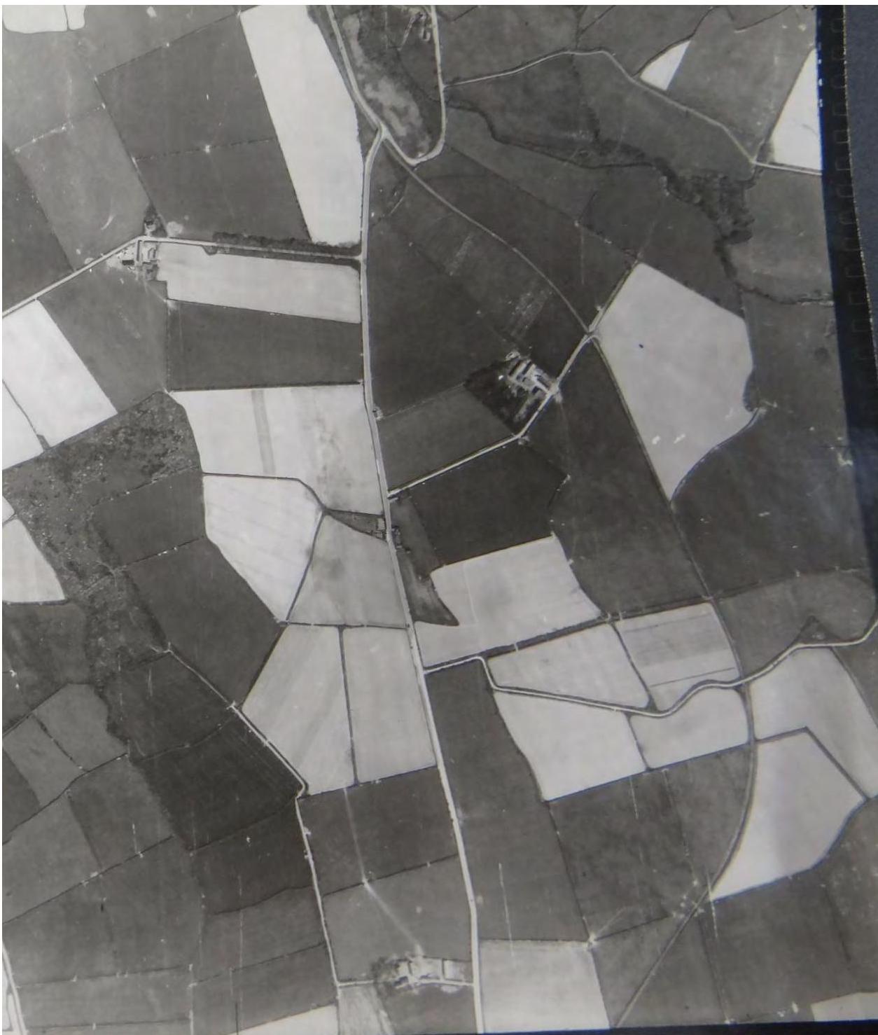 A black and white aerial photograph showing a patchwork of agricultural fields divided by hedgerows and fences.