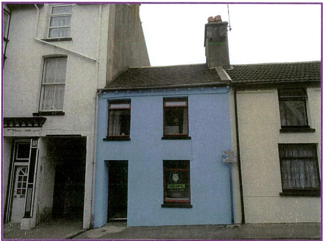 A street-level photograph showing a row of attached buildings, featuring a prominent light blue two-story structure in the center flanked by white buildings.
