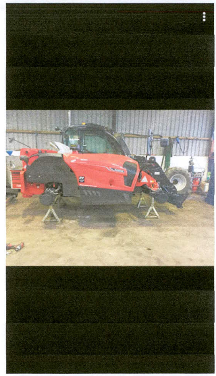 A photograph showing the interior of an agricultural building where a large red tractor is raised on stands for repair.