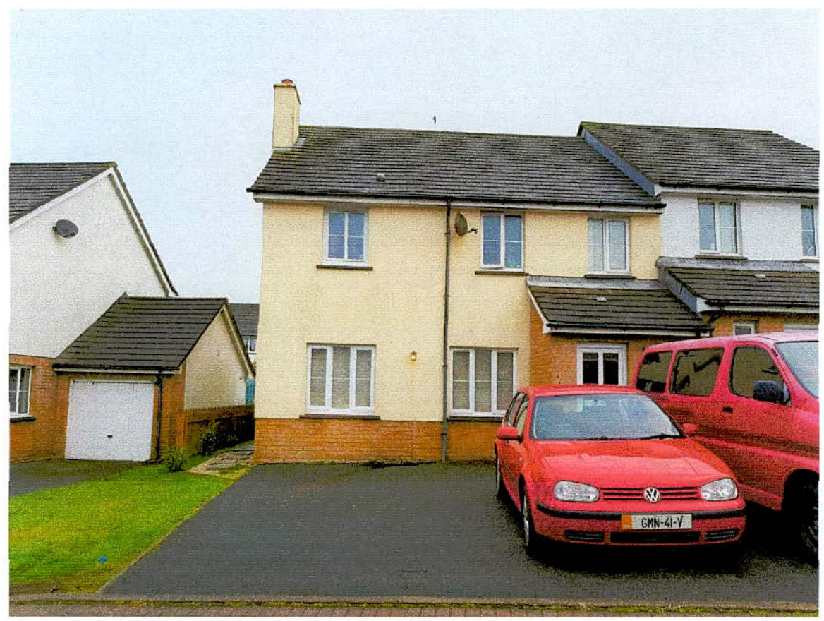 A street-level photograph showing a two-story cream-colored semi-detached house with a driveway and parked red vehicles, likely documenting the existing property for a planning application.