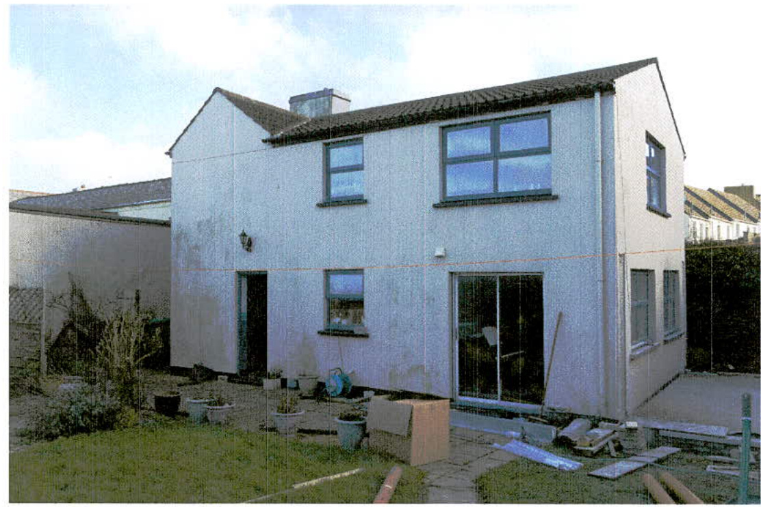 Exterior photograph of a two-story white house showing the rear elevation with a patio area and some construction materials.