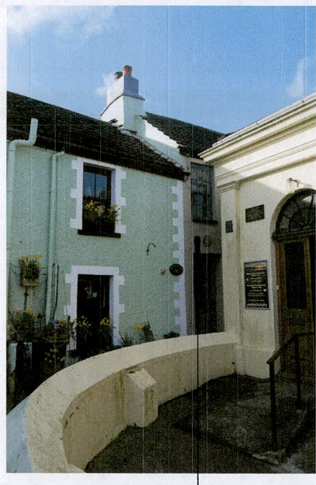 A street-level photograph showing the exterior of a light green terraced building with white quoins adjacent to a cream-colored building with a classical entrance.