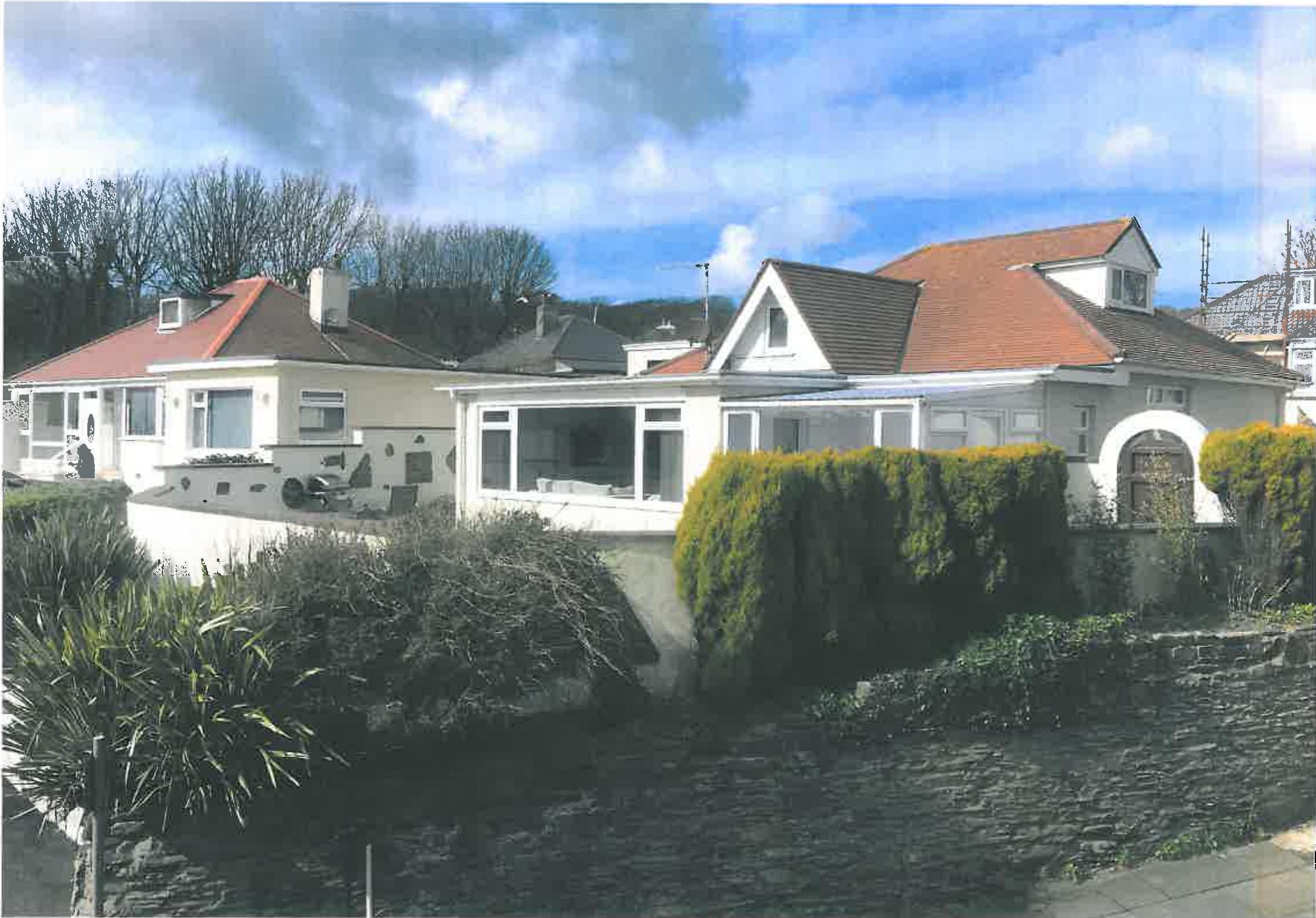 A photograph showing the exterior of a large white detached house with a red tiled roof, featuring a conservatory and surrounding landscaping.