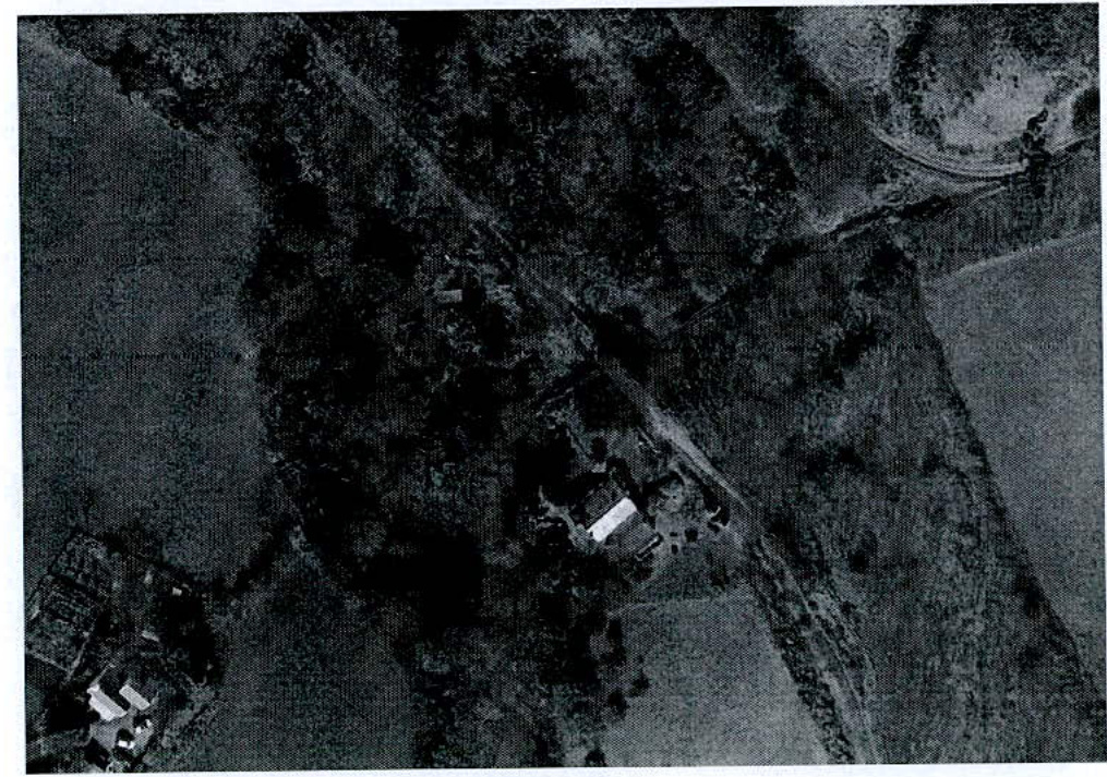 Grainy black and white aerial photograph showing a rural site with fields, hedgerows, and a white rectangular structure.