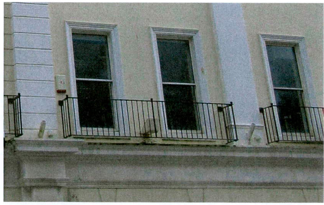 A photograph of a building facade featuring three tall sash windows with black metal railings.