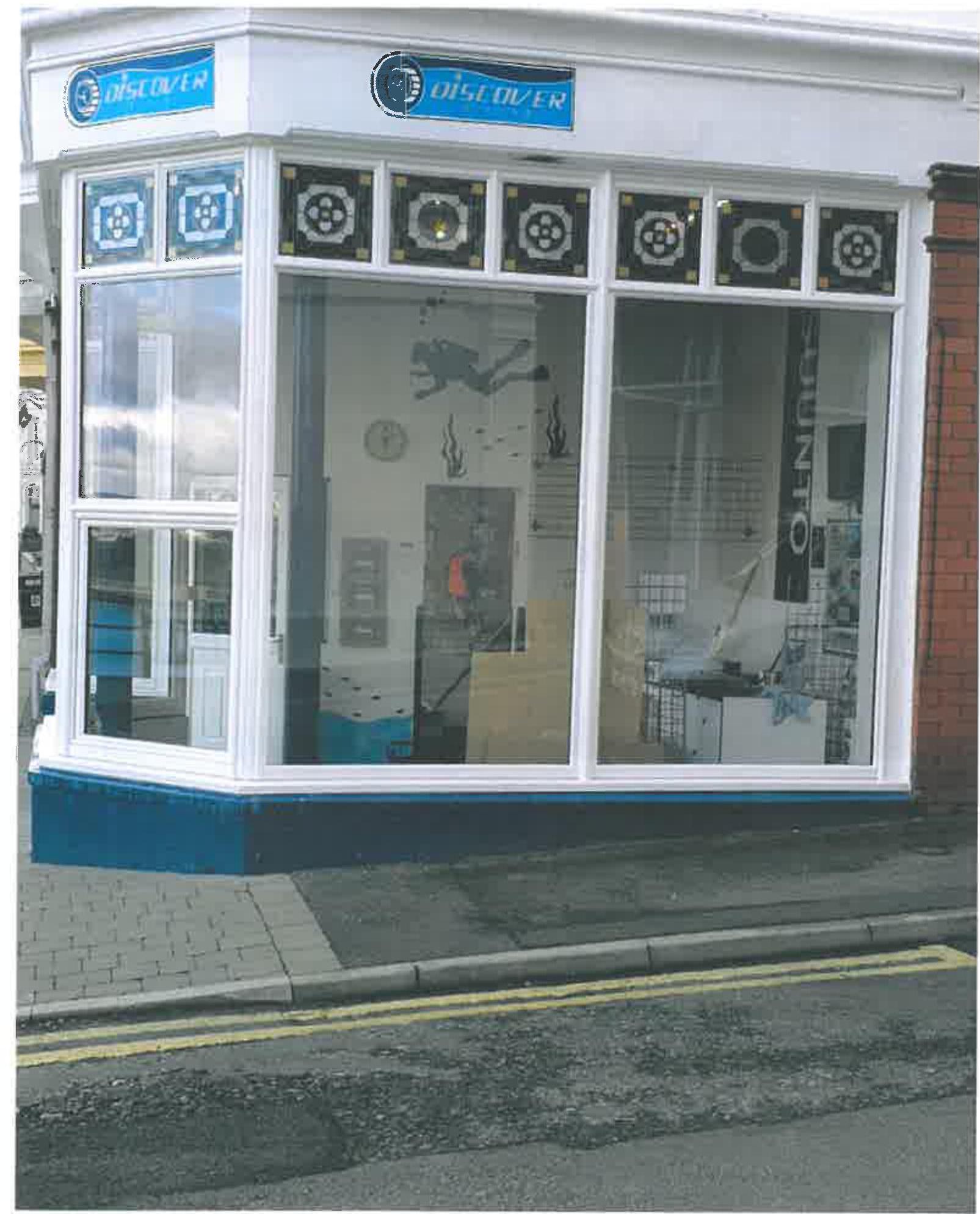 A photograph showing the front elevation of a commercial shop unit with white window frames and decorative stained glass panels above the glazing.