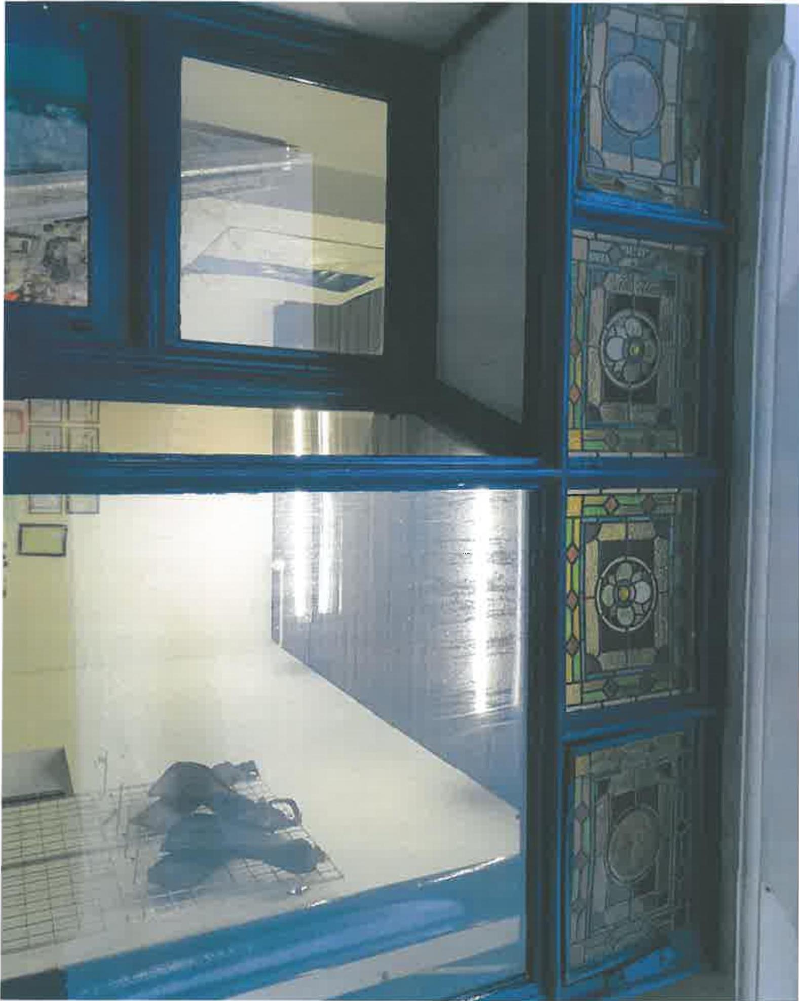 A close-up photograph of a blue-framed window with stained glass panels on the right, showing the interior of a commercial space through the open sash.