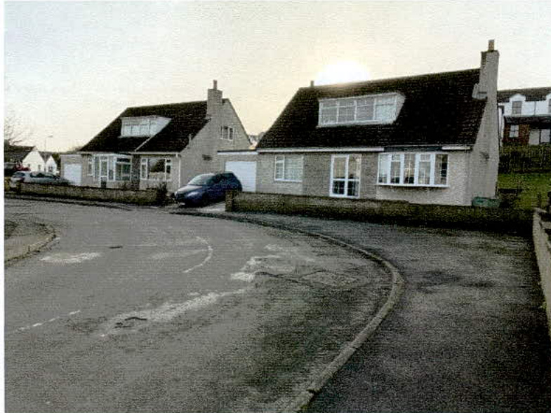 A street-level photograph showing two bungalows with existing driveways and garages along a curved road.