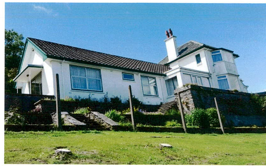 A photograph of a white detached house featuring a tiled roof, stone boundary walls, and a grassy foreground.