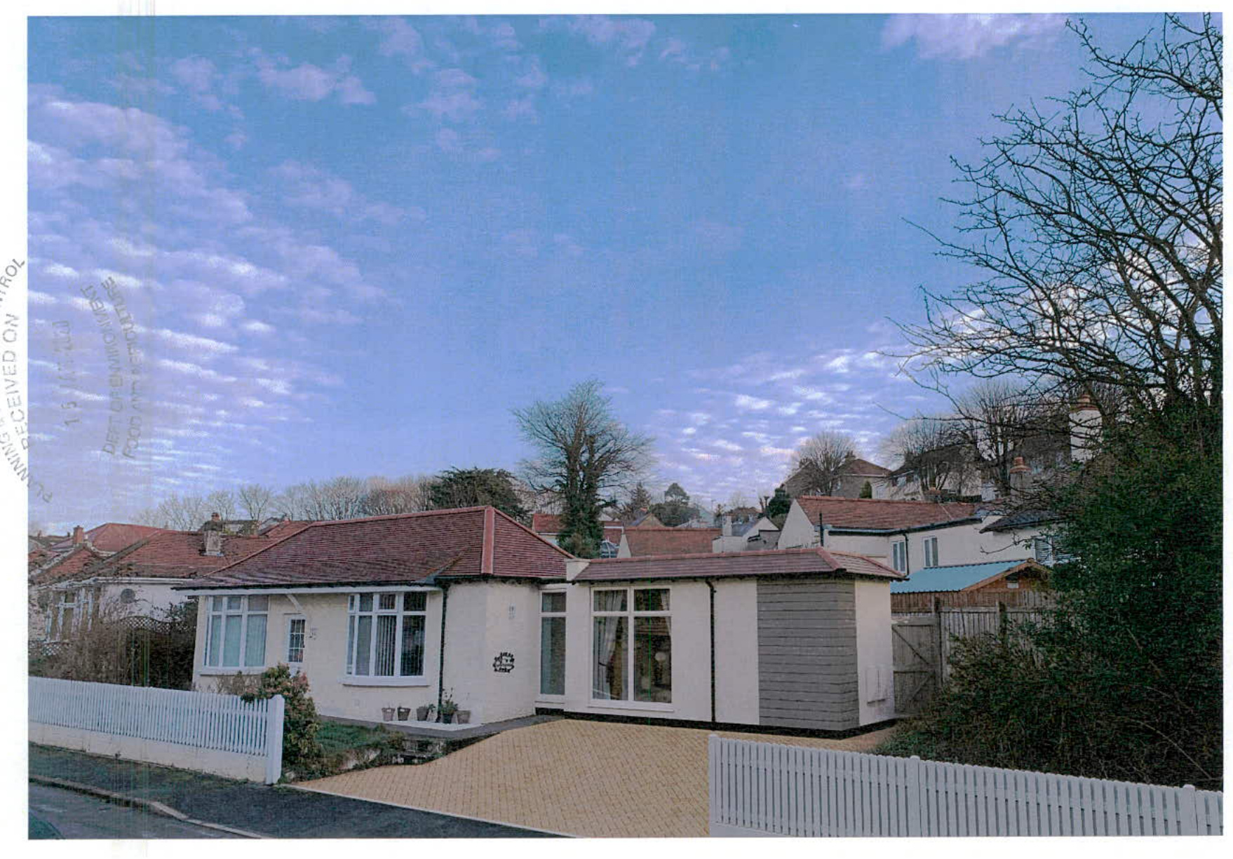 A photograph showing a white single-story bungalow with a prominent side extension featuring large windows and grey cladding.