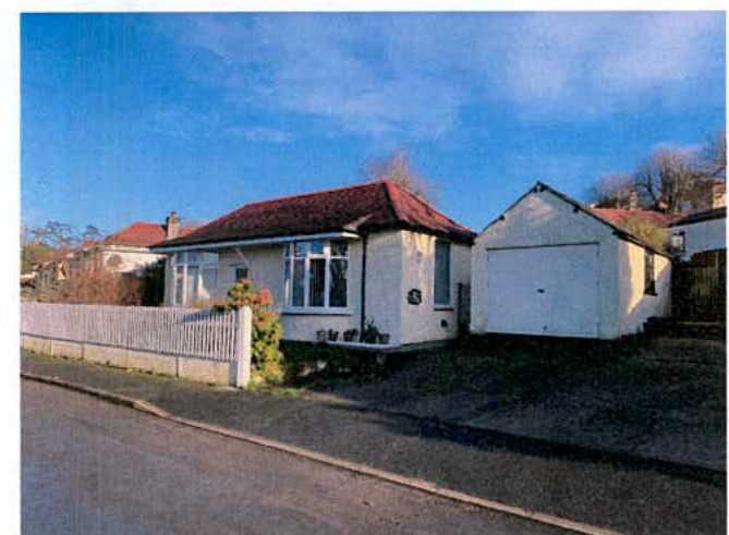 A photograph showing a white single-story bungalow with a red tiled roof and an adjacent white garage.