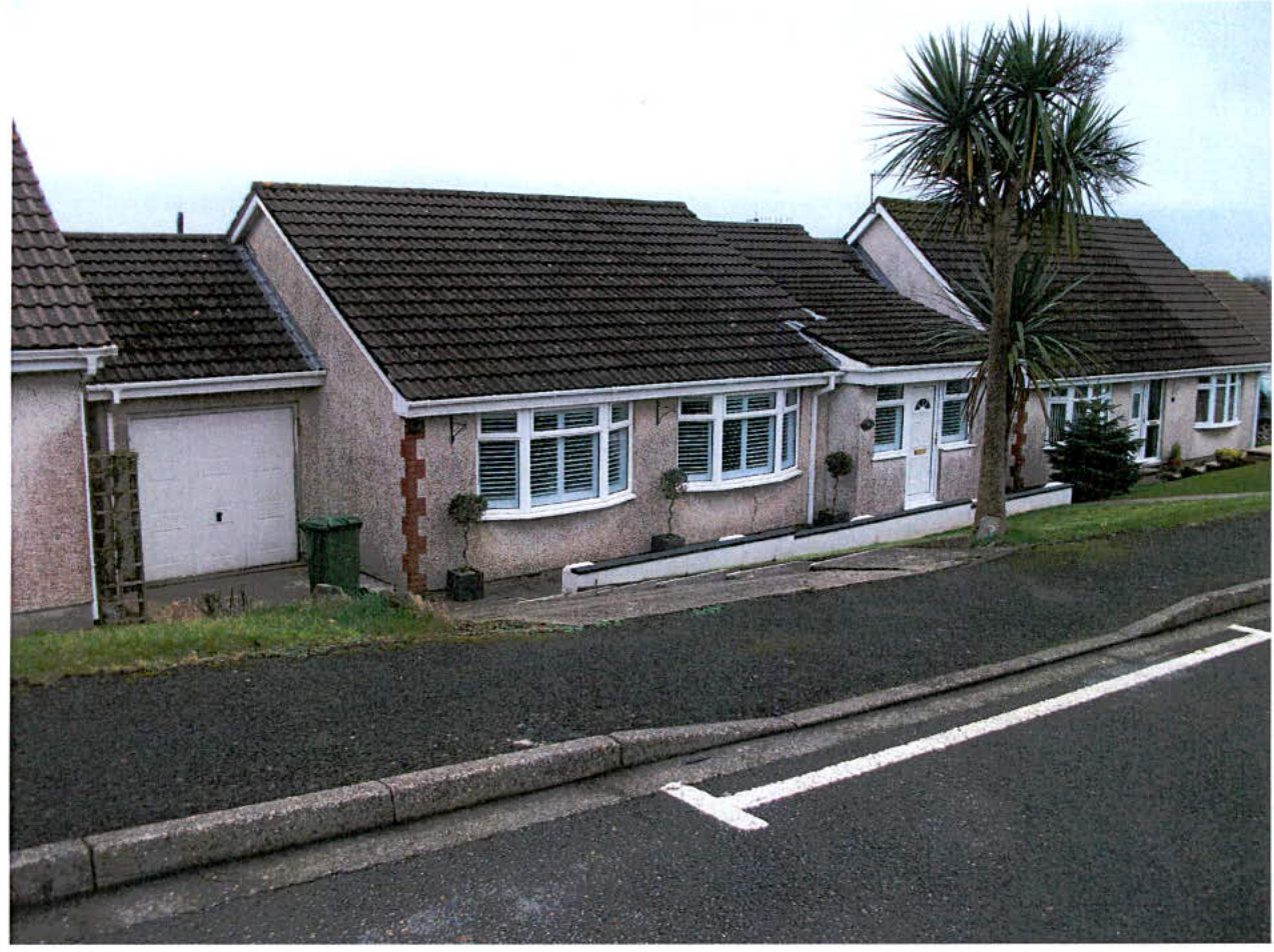 A photograph of a detached bungalow showing the front elevation, garage, driveway, and low boundary wall.