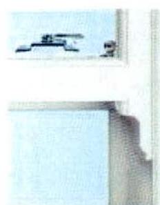 A close-up photograph showing the corner detail of a white window frame, specifically highlighting the locking mechanism and frame profile.