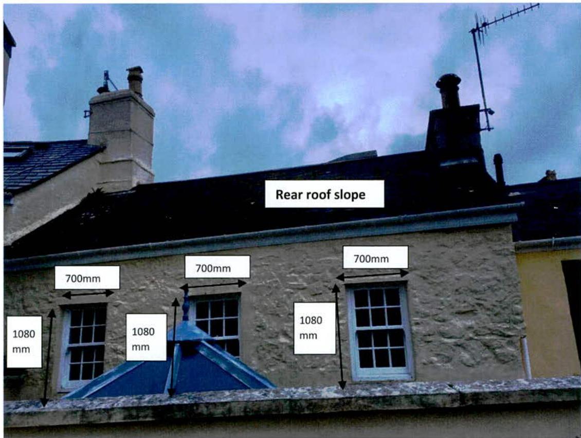 An annotated photograph showing the rear elevation of a stone building with digital callouts indicating window dimensions and roof slope.