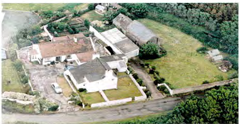 Aerial photograph of a rural property featuring a house, agricultural outbuildings, and a driveway.