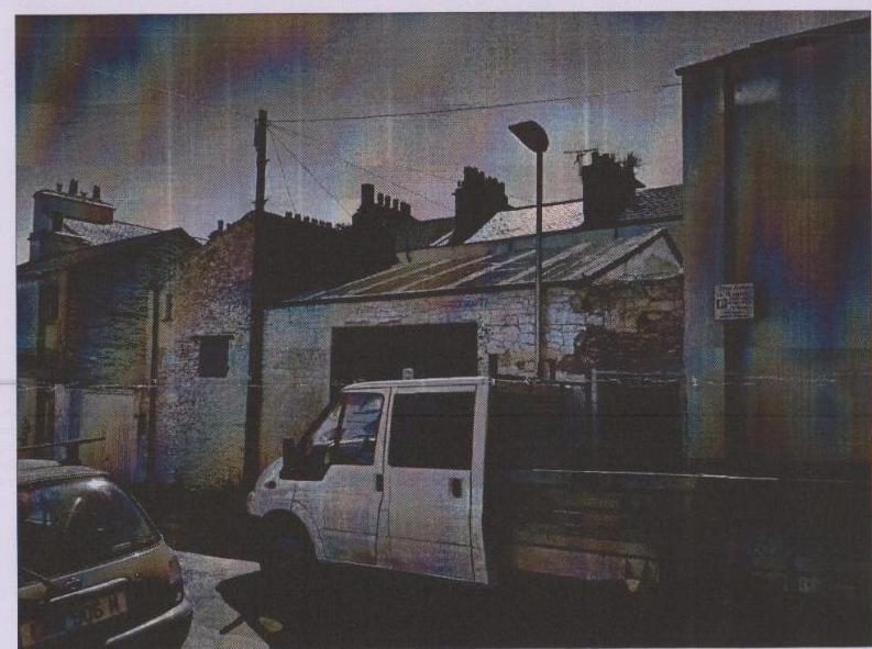 A grainy street-level photograph showing a row of older buildings with a white van parked in front.