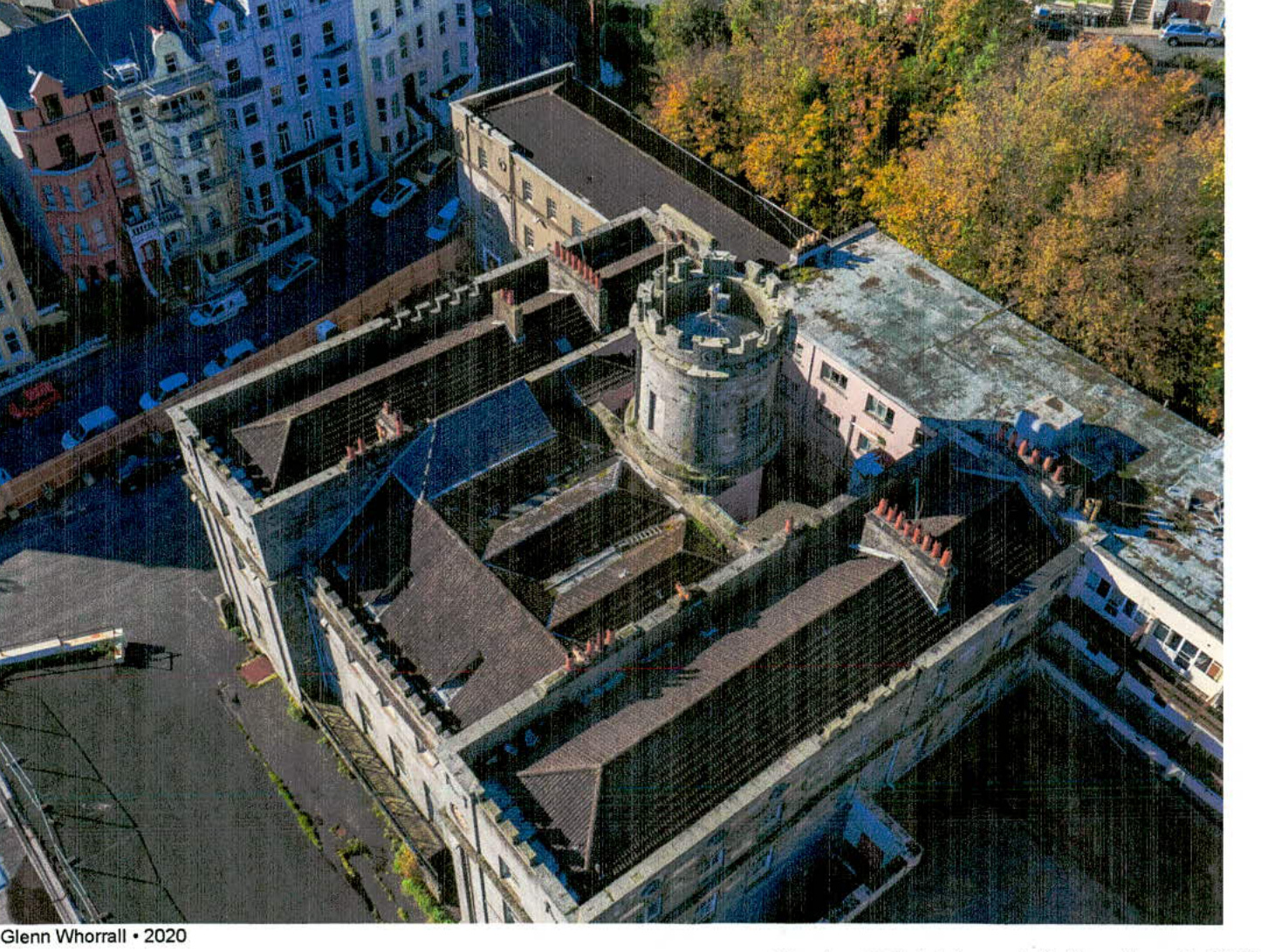 An aerial photograph capturing the complex roof structure of a large historic registered building featuring a prominent stone turret and multiple chimneys.