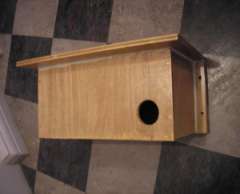 A wooden bird box with a circular entrance hole resting on a checkered tiled floor.