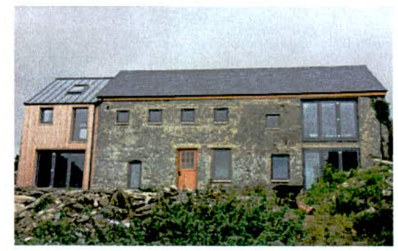 A photograph showing a rural dwelling that appears to be a barn conversion, featuring traditional stone walls alongside a modern timber-clad extension with a metal roof.