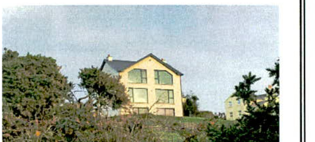 A grainy photograph showing a two-story detached house with large windows situated on a grassy slope surrounded by trees.