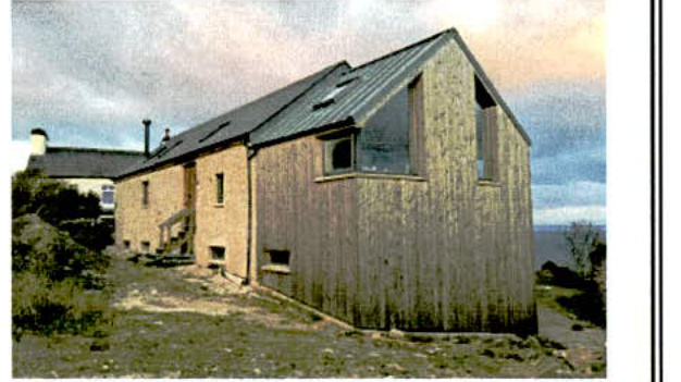 A grainy photograph showing a modern building with mixed brick and wooden cladding and a pitched roof with skylights.