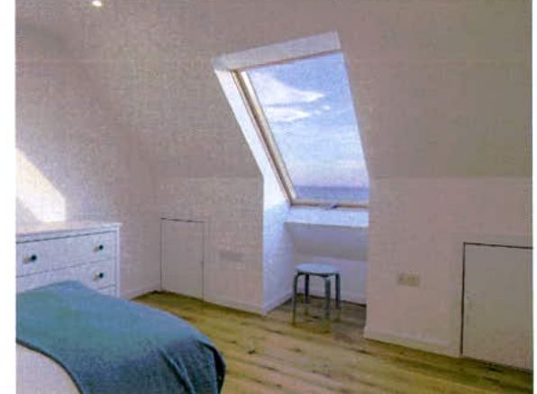 Interior photograph of a bedroom featuring a large skylight window with a view of the sea.